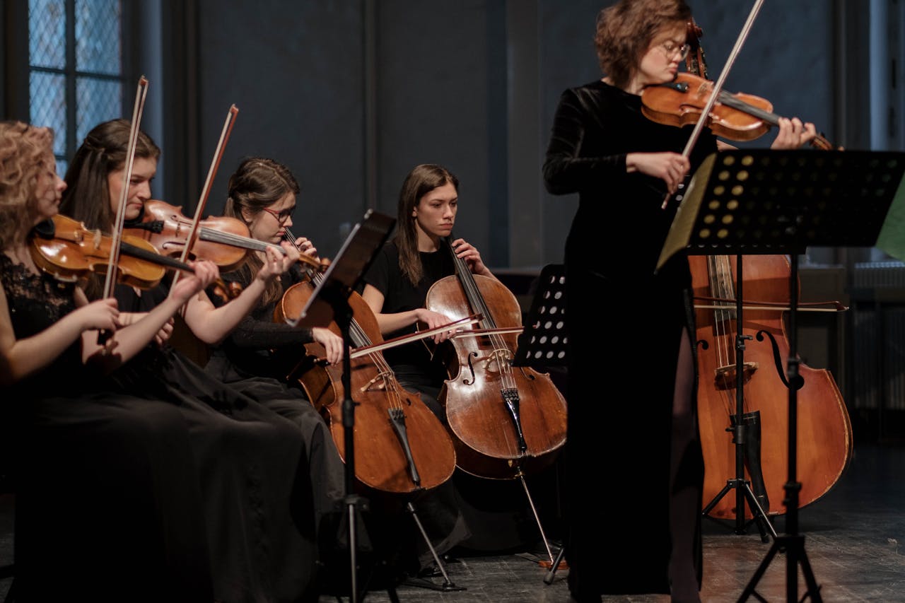 A group of women musicians performing classical music with violins and cellos in an orchestral setting.